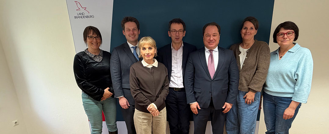 Bild: Dekoratives Bild (Sieben Männer und Frauen stehen lächelnd vor einer Wand)