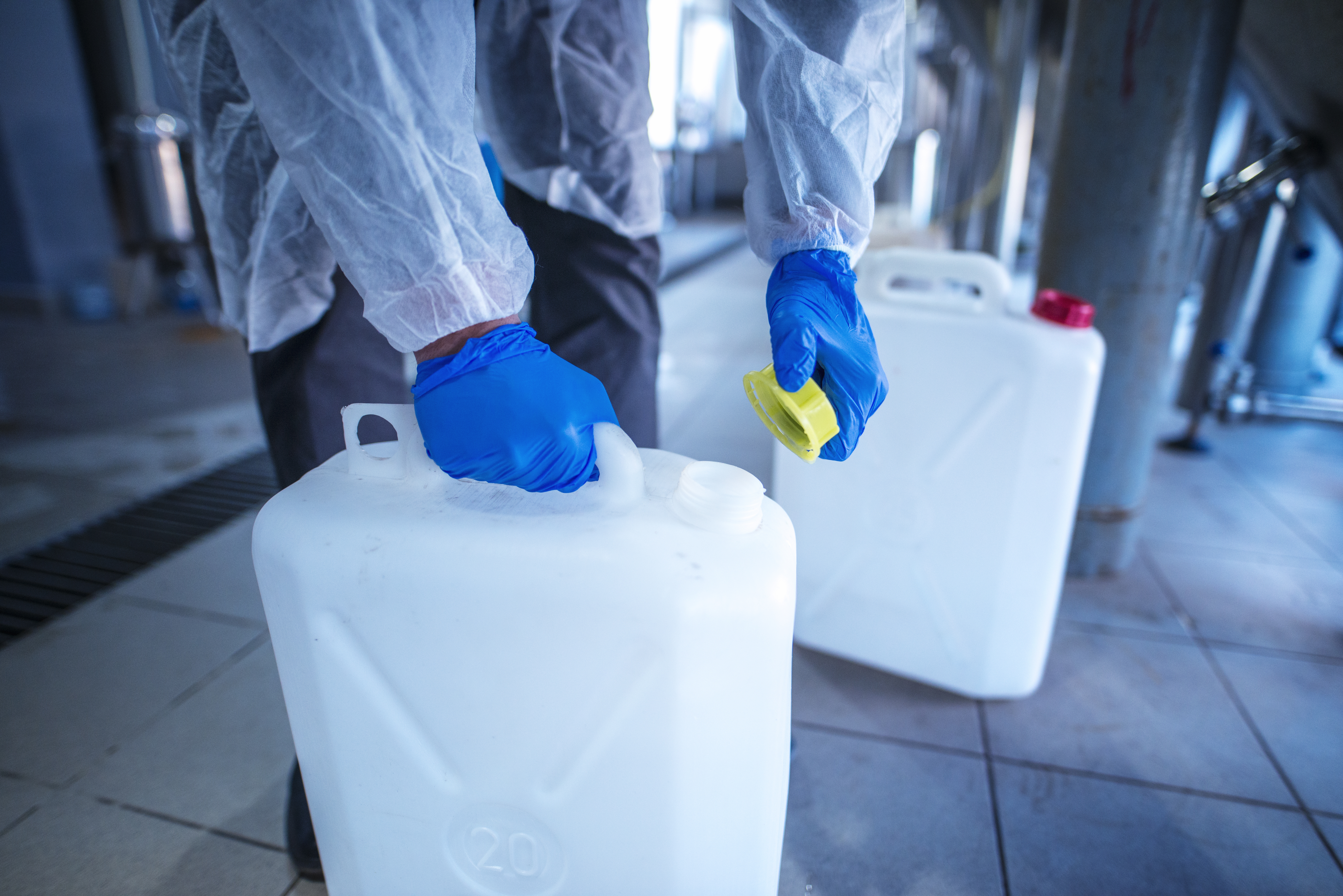 Chemikalien Kanister Gefahrstoffe Zwei Hände von Person in Schutzkleidung fassen weiße Gefahrstoffkanister