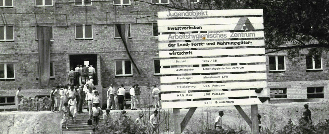 Bild: Auf einer Baustelle vor einem Rohbau: Eine Menschenmenge betritt ein Gebäude mit einem Richtkranz, davor ein Schild zum Investvorhaben. Zur Meldung: Vor 40 Jahren: Richtfest des heutiges LAVG-Hauptsitzes.