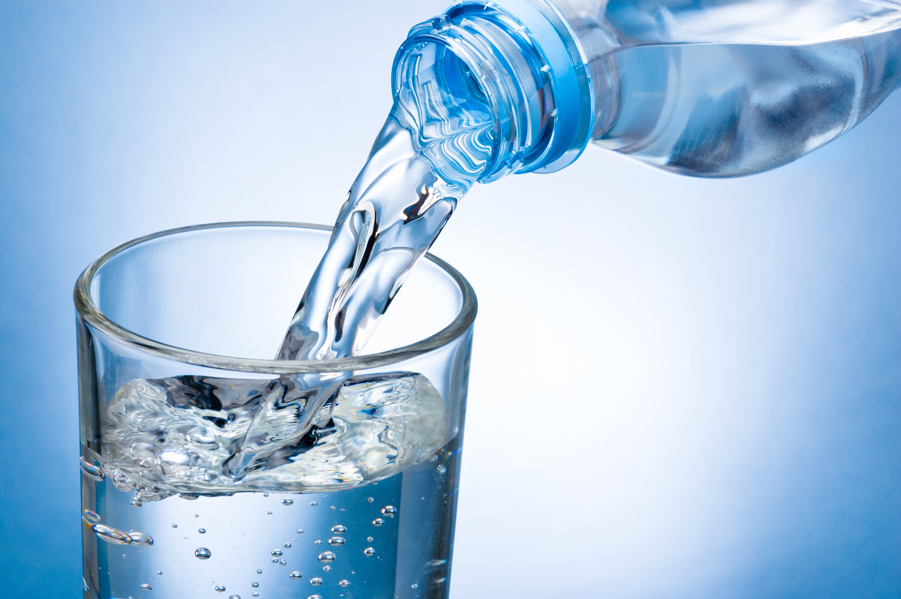 Wasser fließt aus einer Flasche ins Glas, blauer Hintergrund
